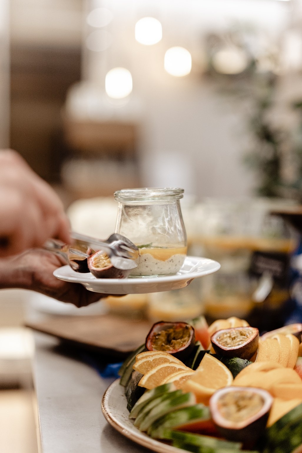 Klaaspurgis magustoit väikesel taldrikul, taustal puuviljavaagen kus on kannatusviljad ja melonid.