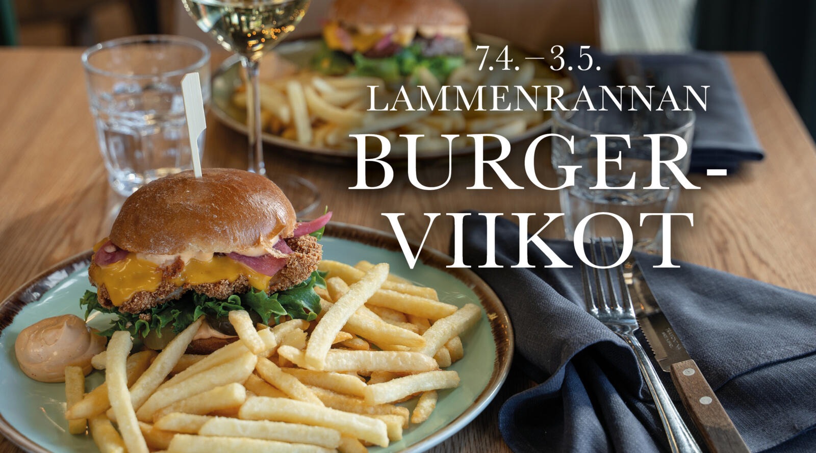 Mehevä ja juustoinen burger lautasella ranskalaisten kanssa. Taustalla näkyy toinen burgerannos eri pihvillä.