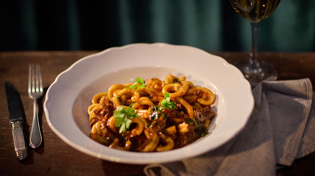 Vit tallrik fylld med calamari-pasta eller bläckfiskrätt i tomatsås, garnerad med färska örter.