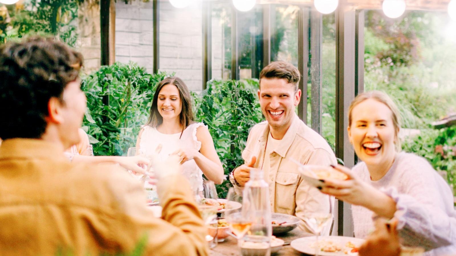 People dining outdoors around a table in a summer setting.