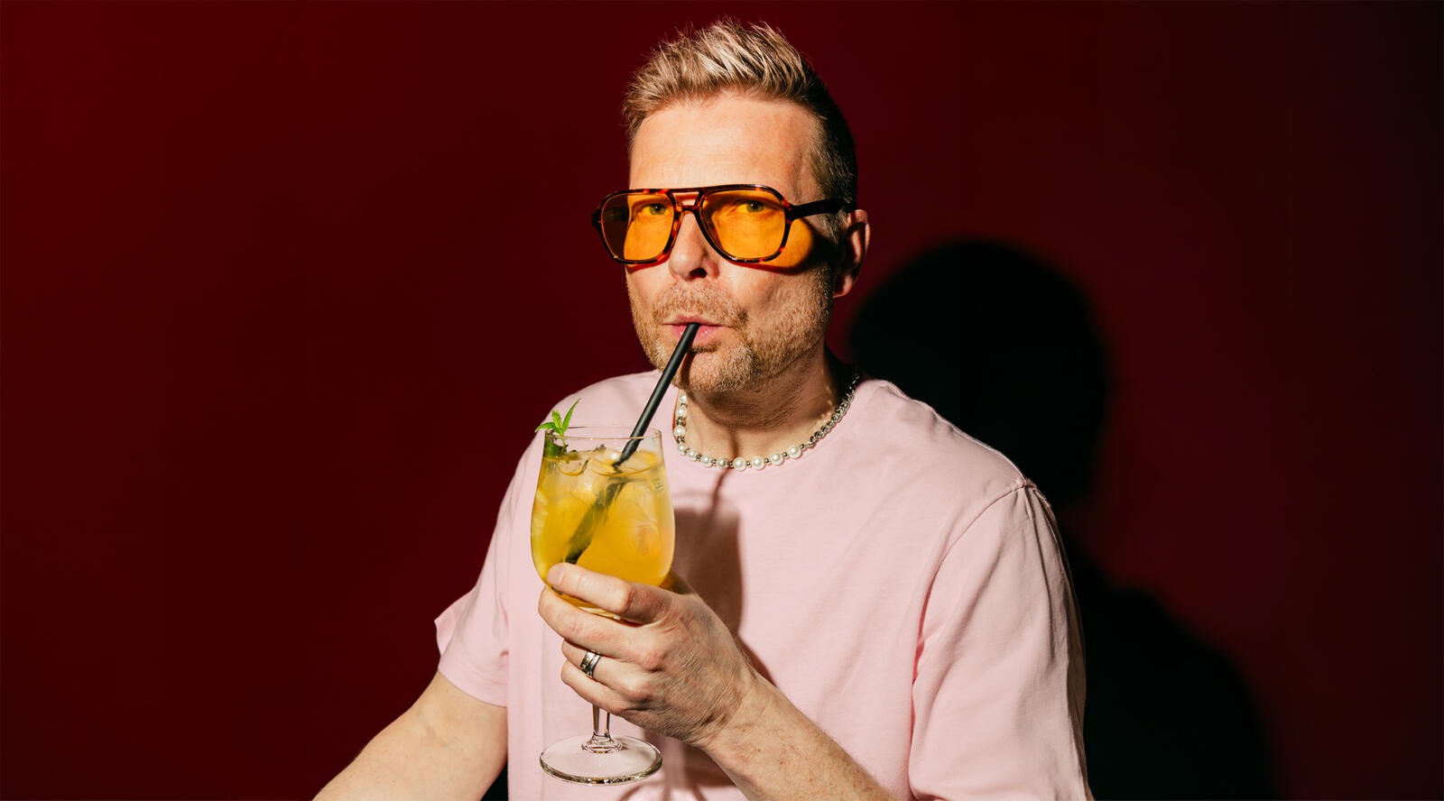 Mies juo pillillä keltaista juomaa lasista terassilla