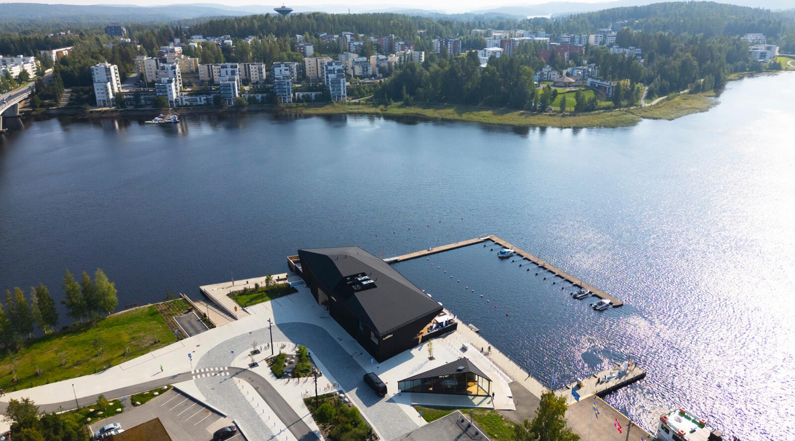 Ilmakuva modernista rakennuksesta järvenrannalla, tasaisella piha-alueella ja laiturilla.