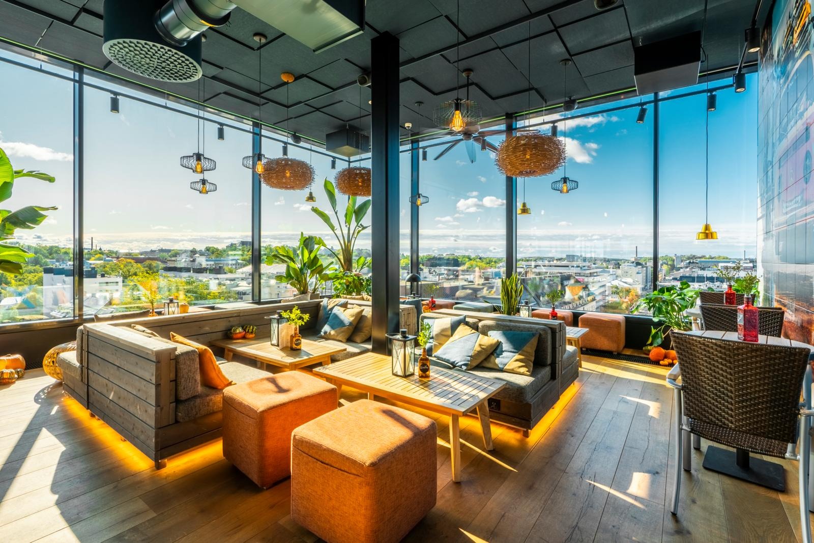 Mysig takrestaurang med stora fönster, gott om naturligt ljus, gröna växter och panoramautsikt över staden. Trägolv och moderna möbler.