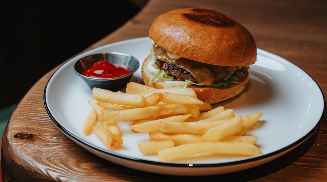 Ostburgare och pommes frites på en vit tallrik, med ketchup i en liten stålskål.