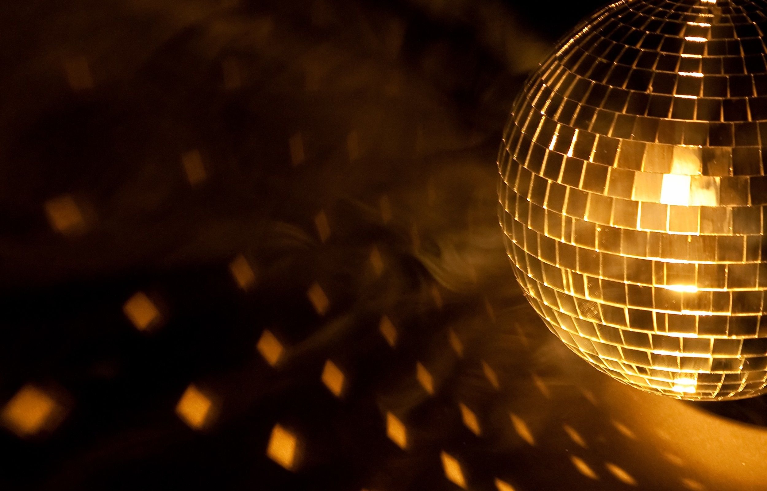 Kultainen diskopallo heijastaa kimaltelevia valolaikkuja tummaan tilaan.