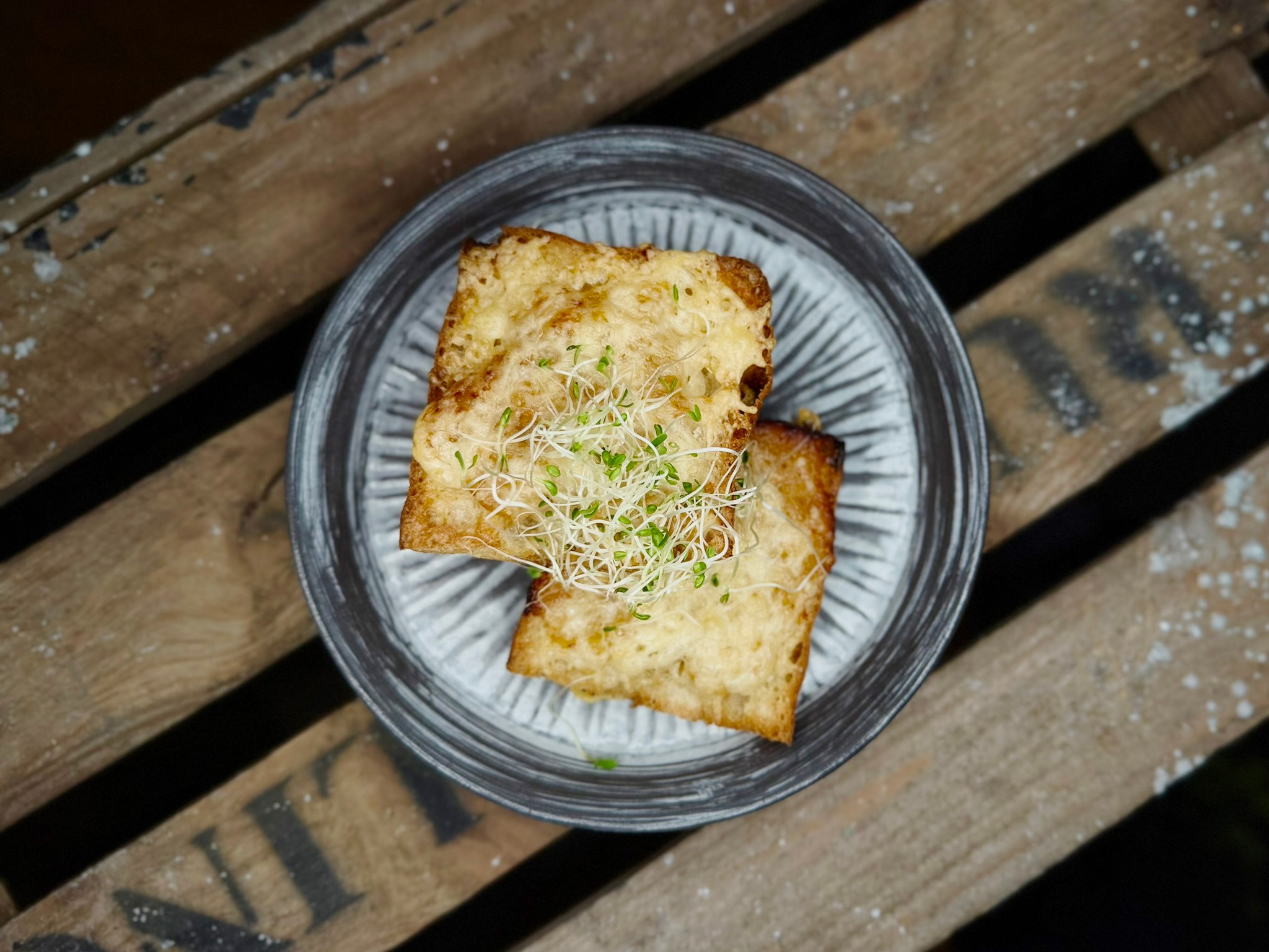 A slice of toasted bread topped with microgreens, served on a plate atop a wooden surface.