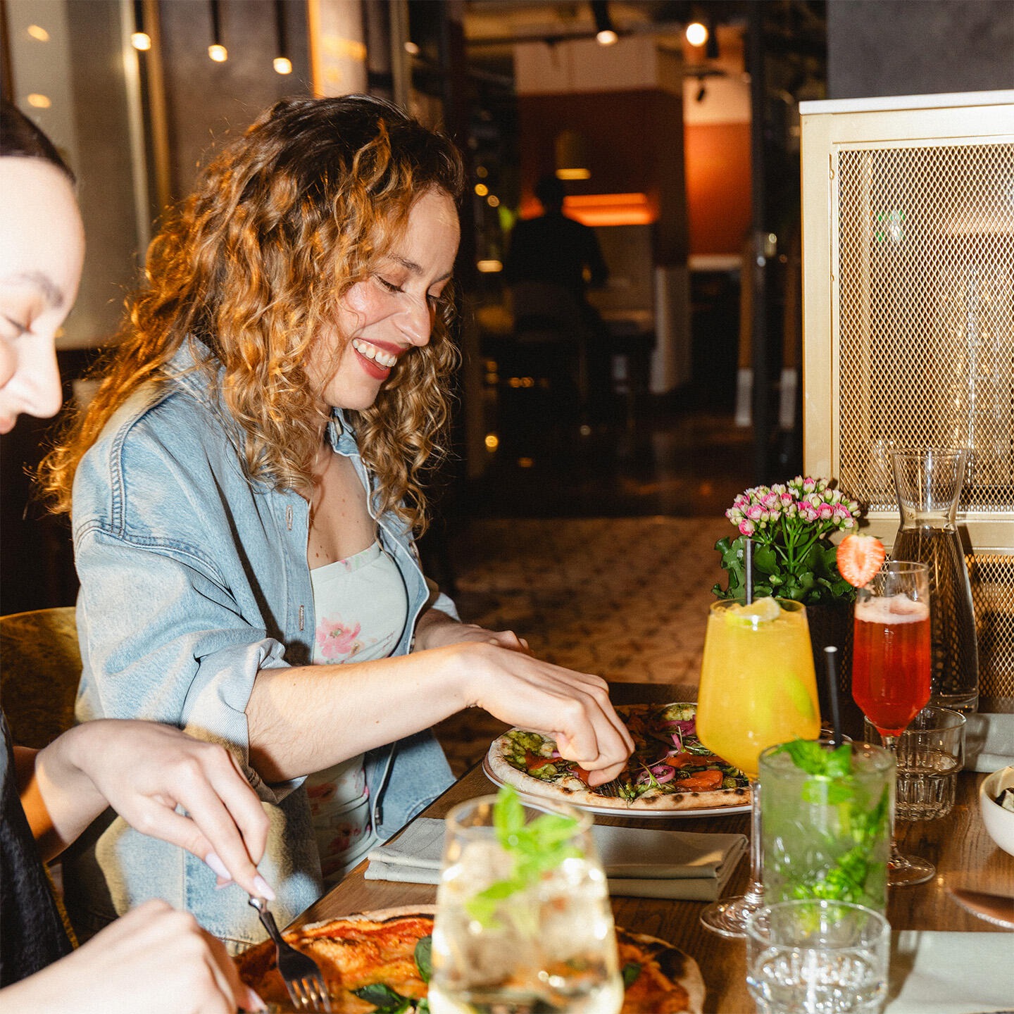 Restaurangbord med flera maträtter och cocktails. Inomhusmiljö med glasdörrar och dekorationsljus i bakgrunden.
