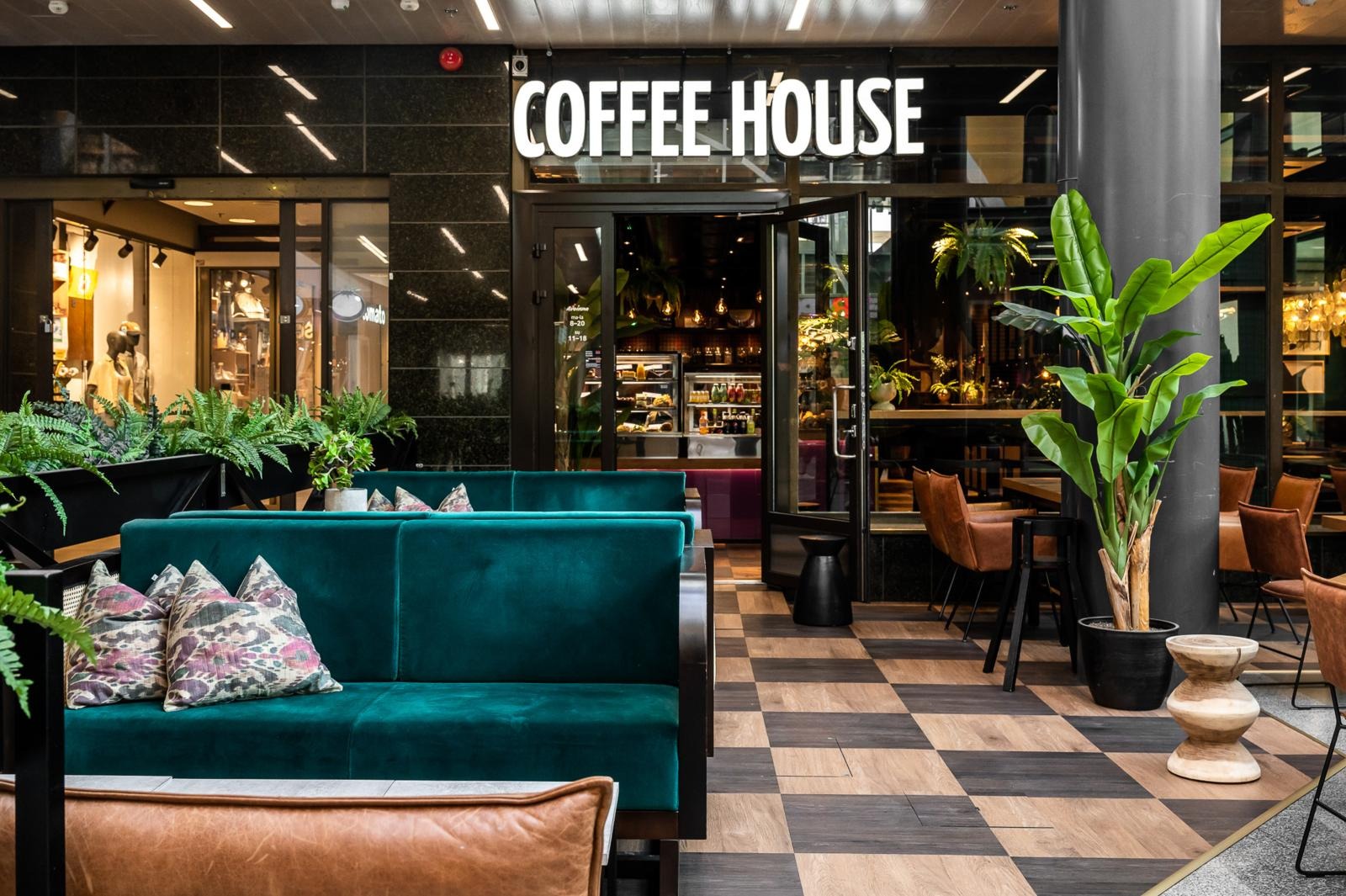 Coffee Housen sisäänkäynti ja terassimainen alue kauppakeskuksen sisällä, jossa asiakkaat voivat nauttia rennosta tunnelmasta.