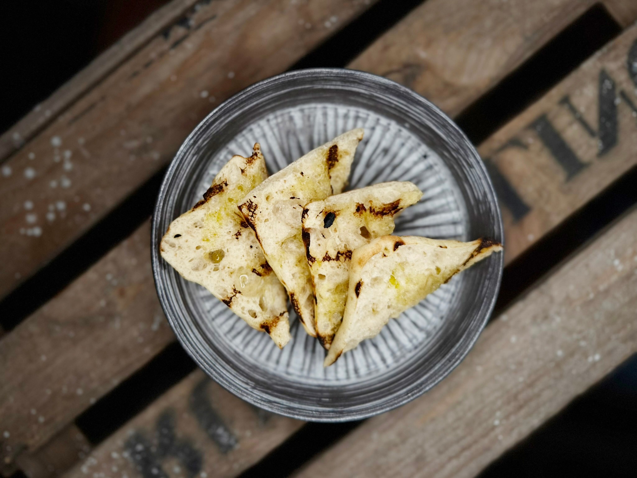 Bowl of triangular toasted bread pieces arranged on a small plate placed on a wooden surface.