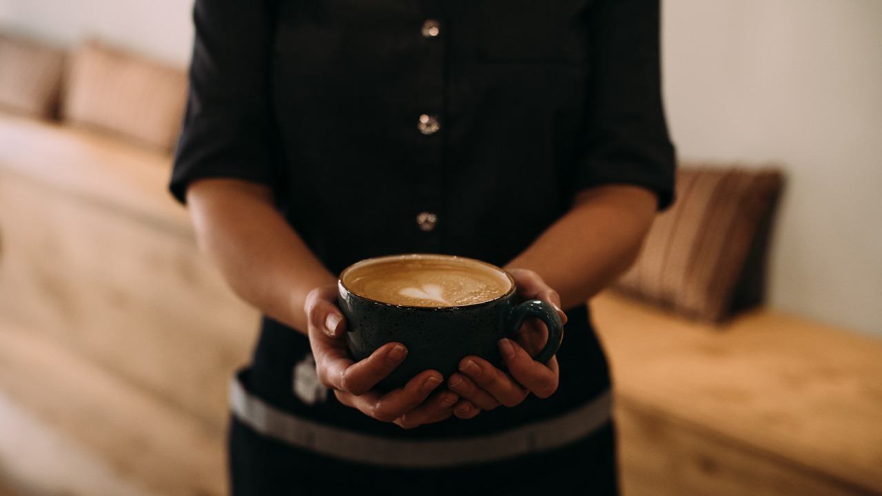 Kahvilan työntekijä pitelee cappuccinoa kädessään.