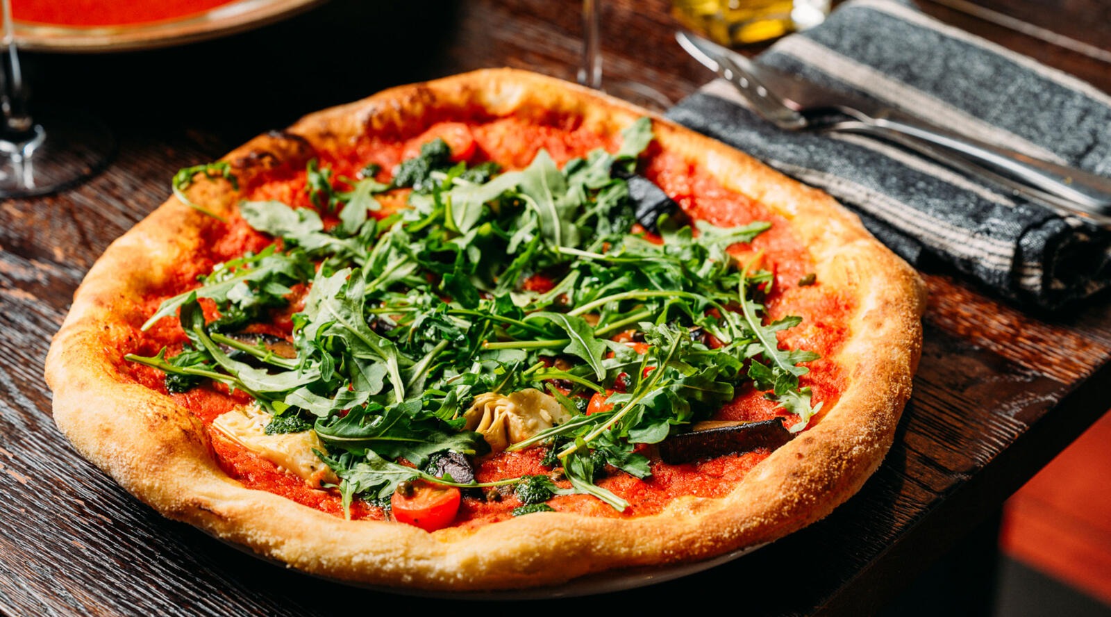 Pizza rucola-täytteellä puupöydällä. Vieressä harmaita servetit ja juoma.