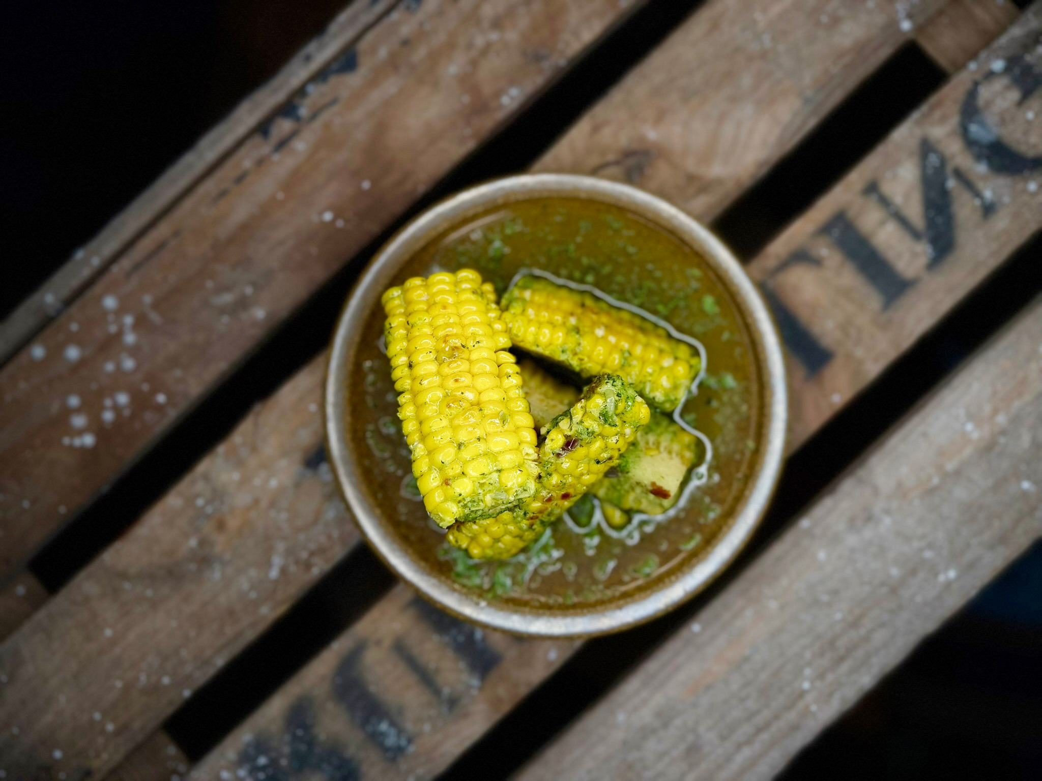 Corn cob pieces in green sauce served in a bowl on wooden slats.