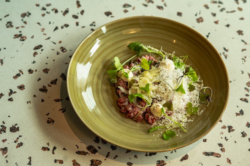 Vihreä keraaminen kulho, jossa tartar-annos koristeltuna yrteillä ja parmesaanilla.