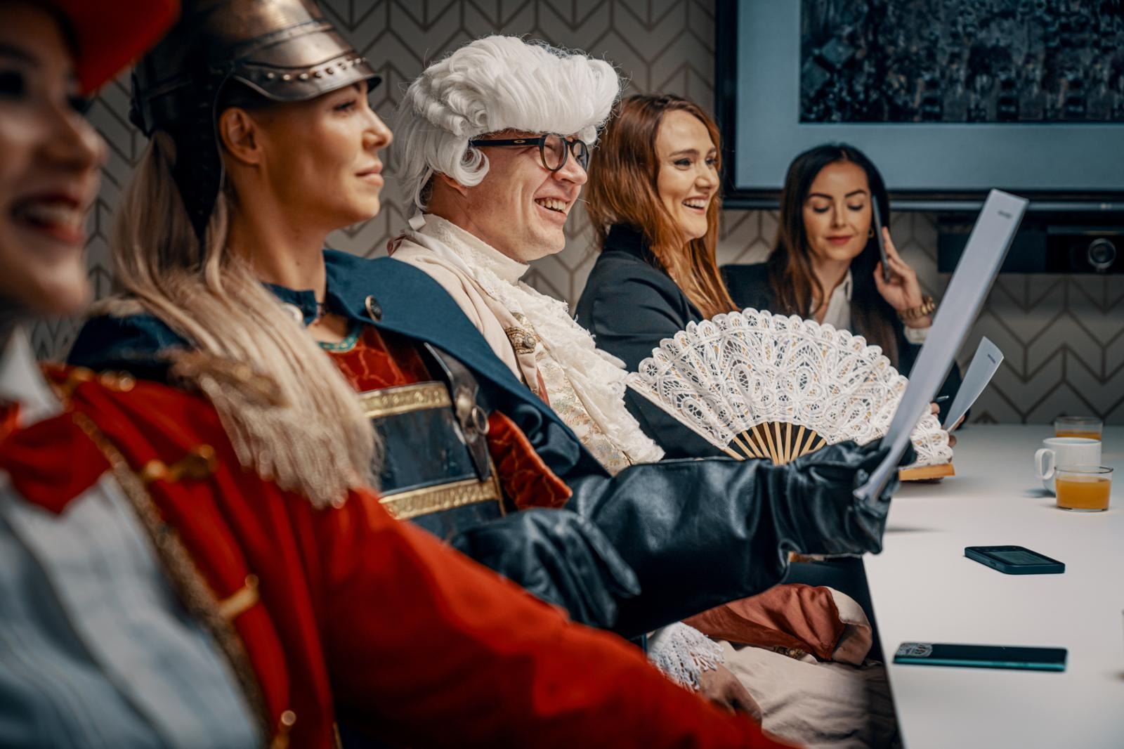 Fem personer sitter runt ett bord, några i historiska dräkter, arbetar med bärbara datorer.