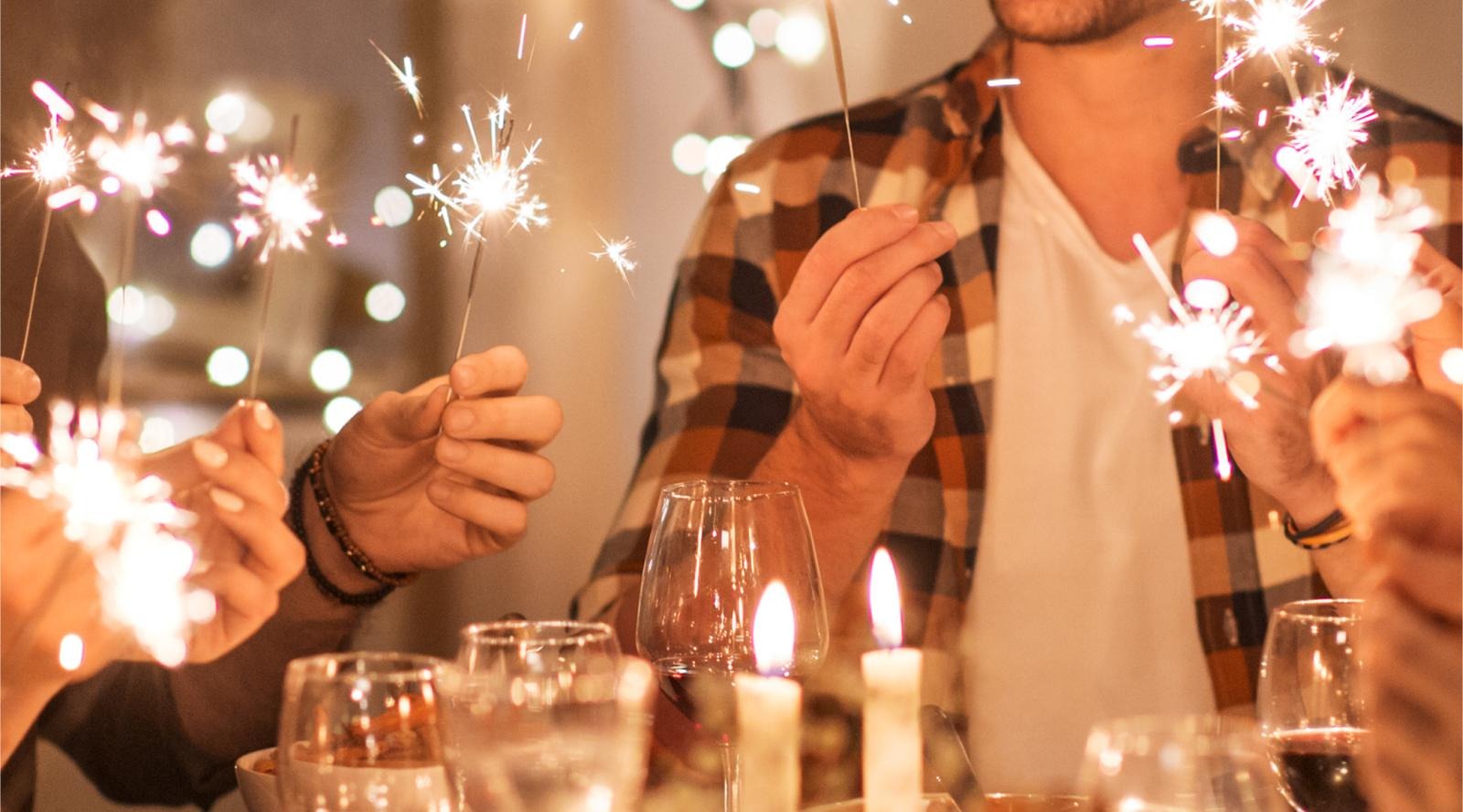 People holding lit sparklers in a festive atmosphere, with candles and wine glasses on the table.