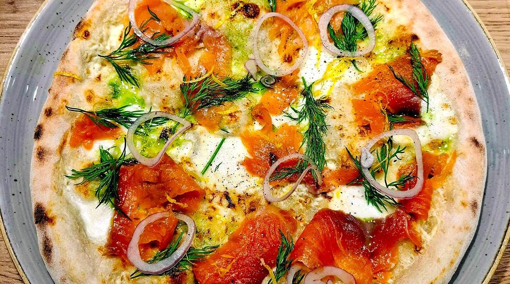 Pizza, jossa lohta, sipulirenkaita ja tilliä kermaisen kastikkeen päällä, tarjoiltuna harmaan lautasen päällä.