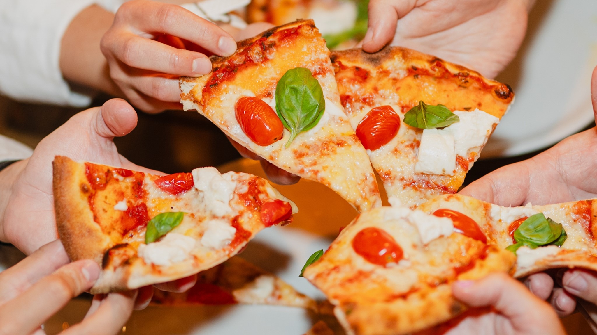 Hands holding pizza slices with tomato, mozzarella and basil.