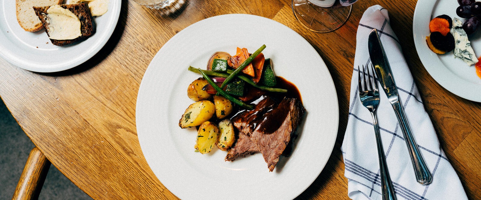 Table with plate of steak dish, potatoes and vegetables. Wooden table surface.