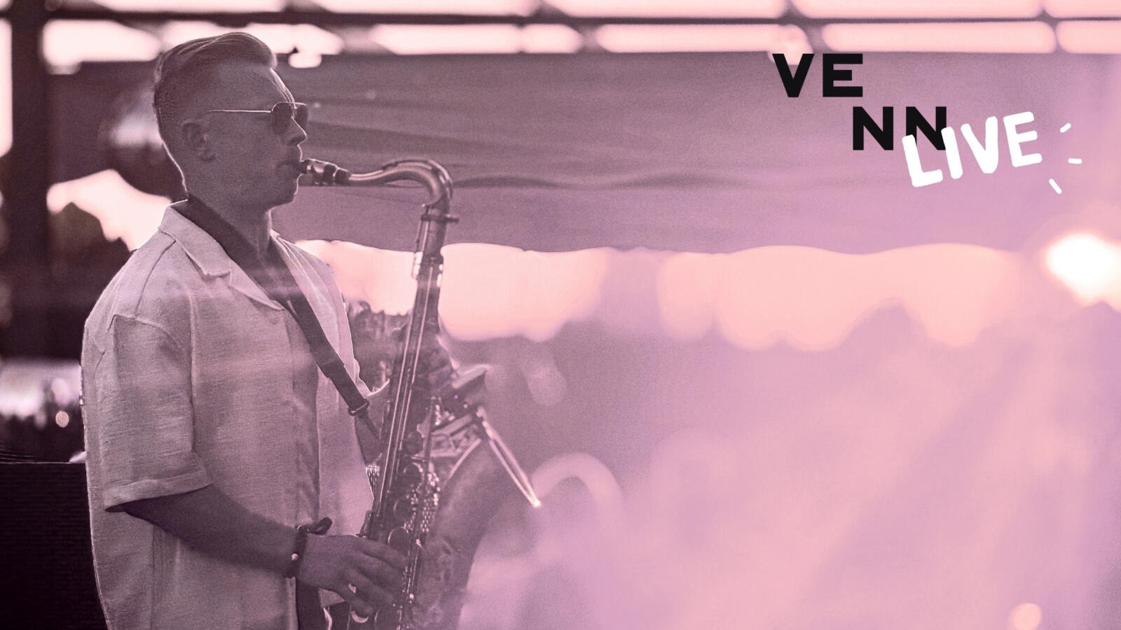 Saxophonist performing outdoors at dusk, water and lighting decoration in the background.