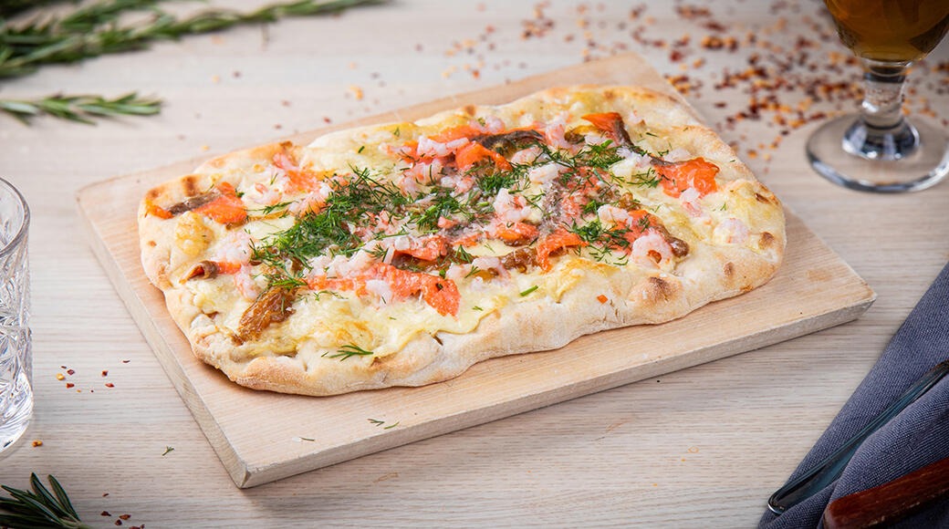 Leipäpohjainen pizza lautasella, päällä lohta, tuorejuustoa ja tilliä.
