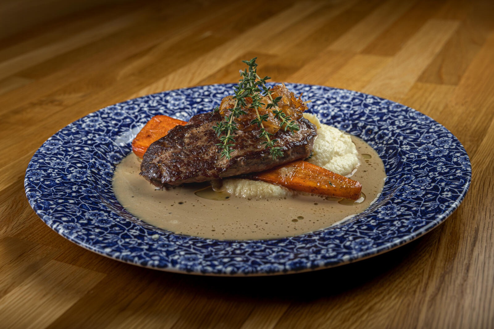 Tallrik med stekt kött, rostade morötter och potatismos i brun sås, garnerad med timjan.