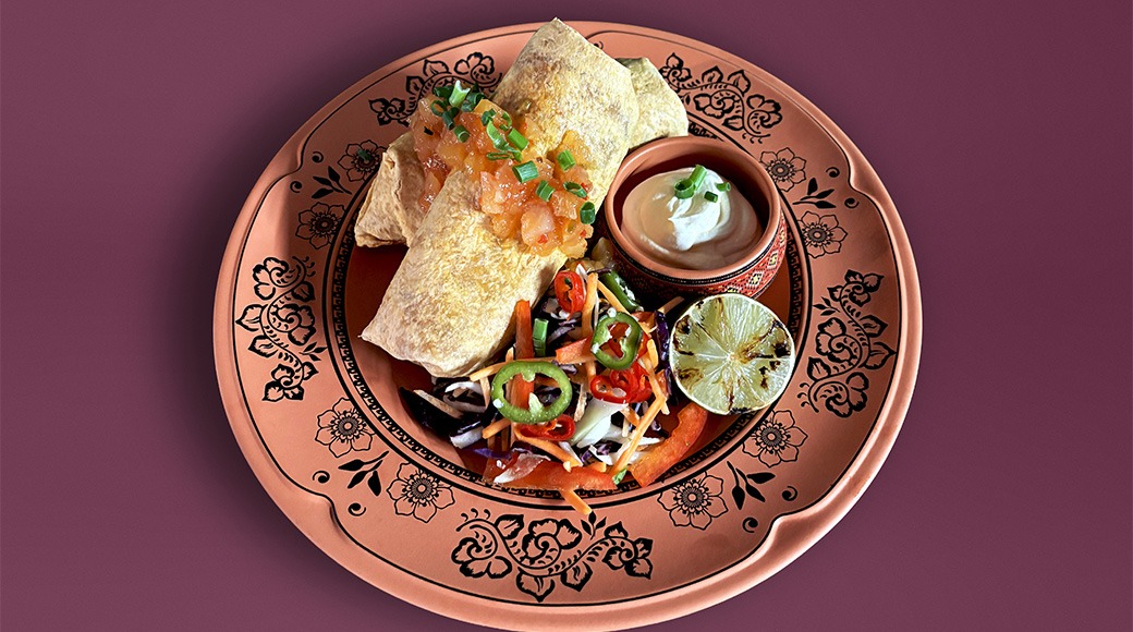 Tortilla meal served on decorative copper-colored plate with fillings, colorful coleslaw salad, lime wedge and small bowl of creamy sauce.