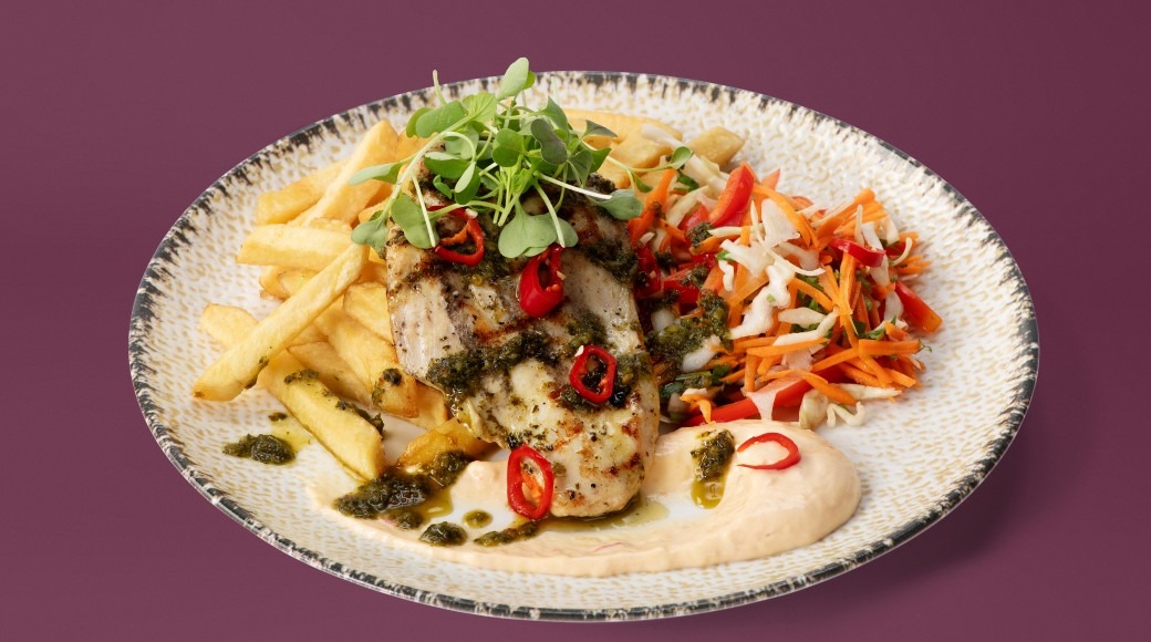Plate with grilled fish, french fries and fresh vegetables against burgundy background.