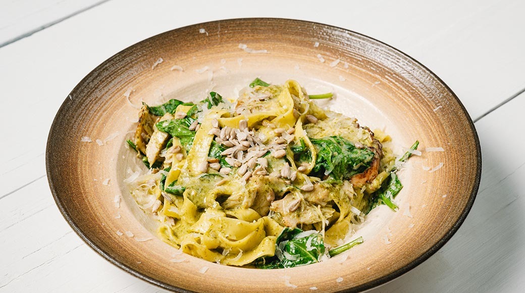 Lai pasta pestokastmes spinati, kana, päevalilleseemnete ja riivjuustuga pruunis kausis.