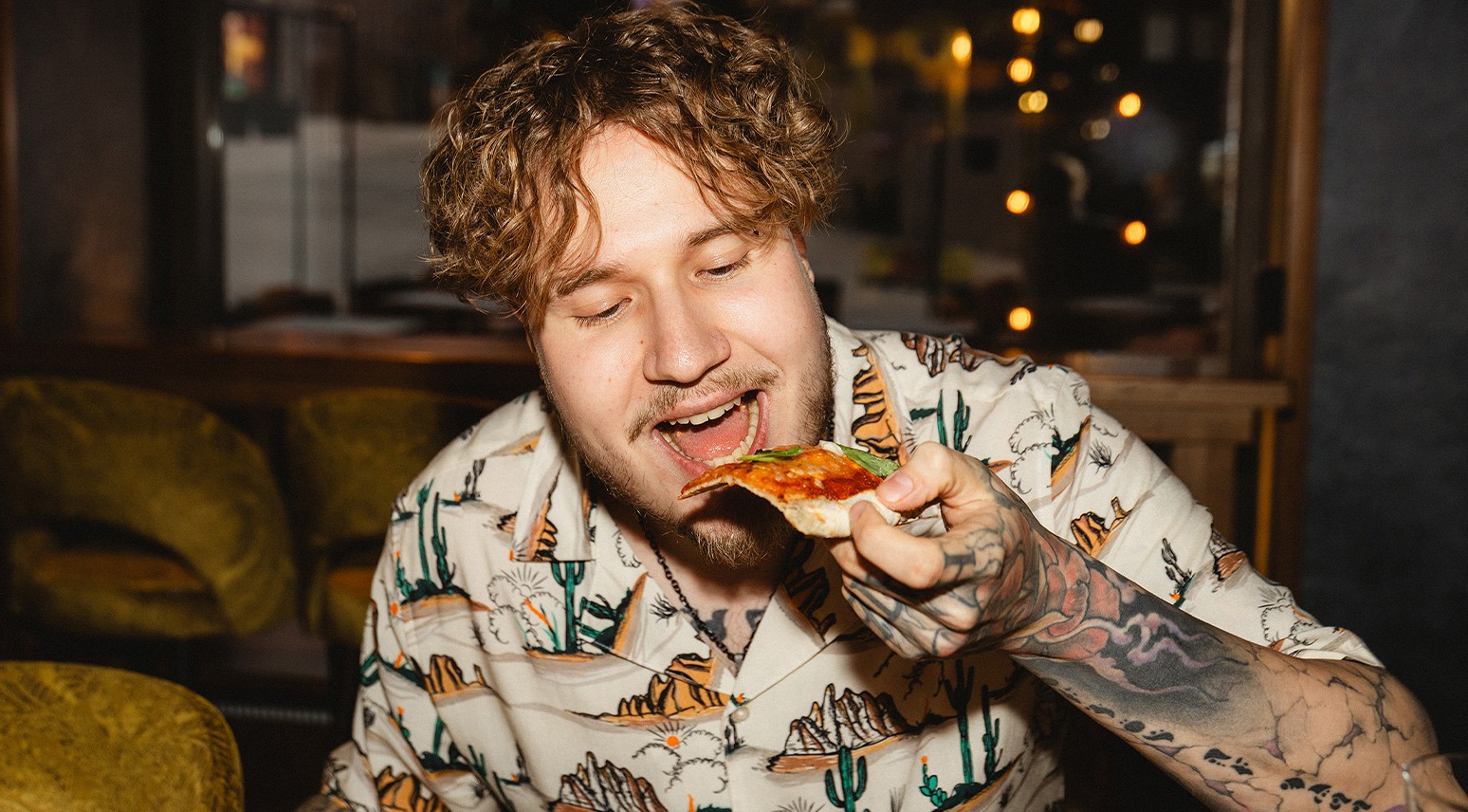Person äter pizza på en restaurang med dämpad stämningsbelysning och bekväma gyllengula soffor.