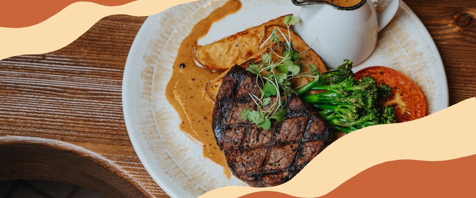 Annos grillattua pihviä, paistettuja perunoita, parsakaalia ja tomaattia valkoisella lautasella ja kastikkeella.