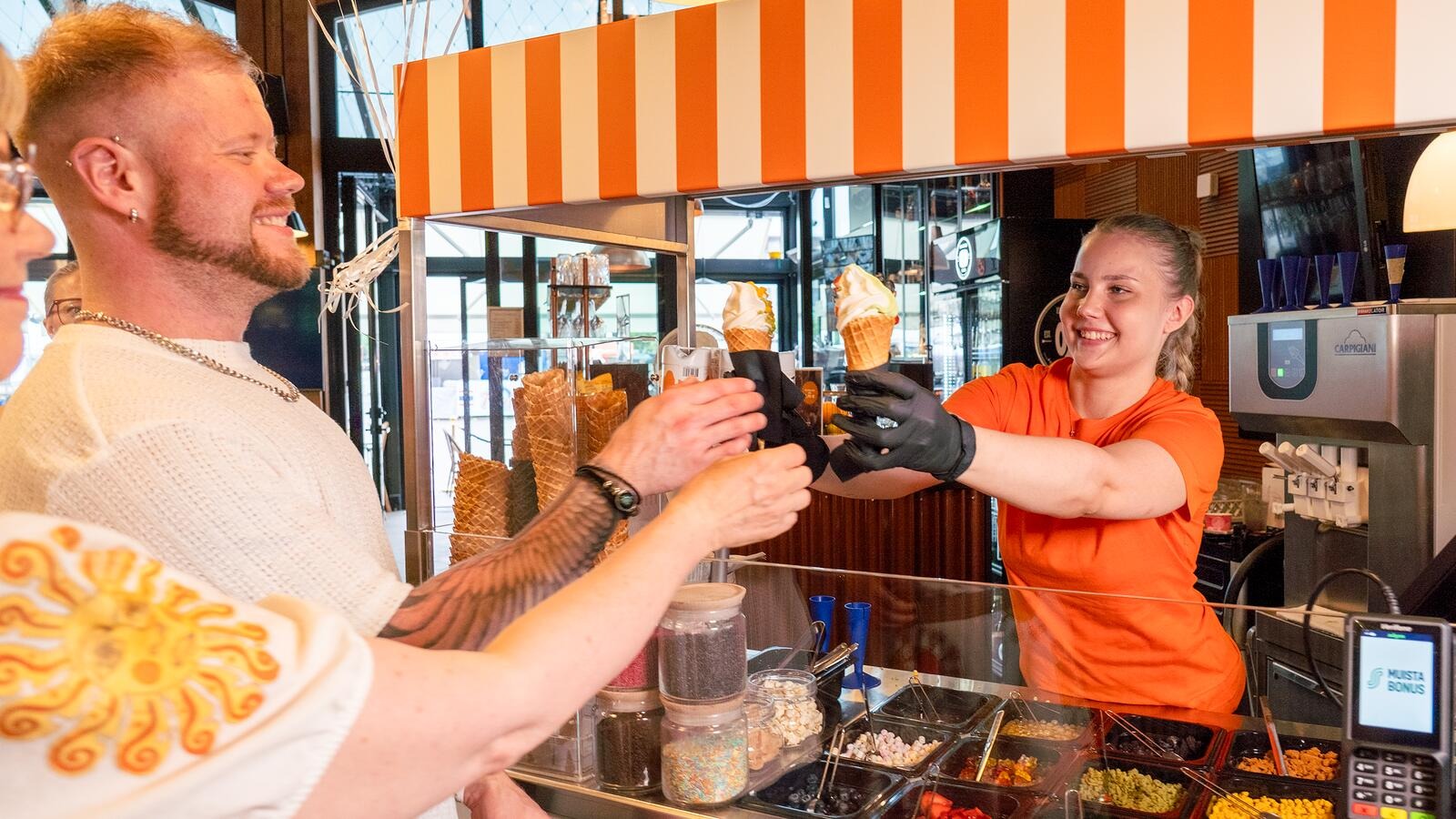 Kauppahalli Joensuun pehmojätski-kioskin myyjä ojentaa pehmojätskejä asiakkaille.