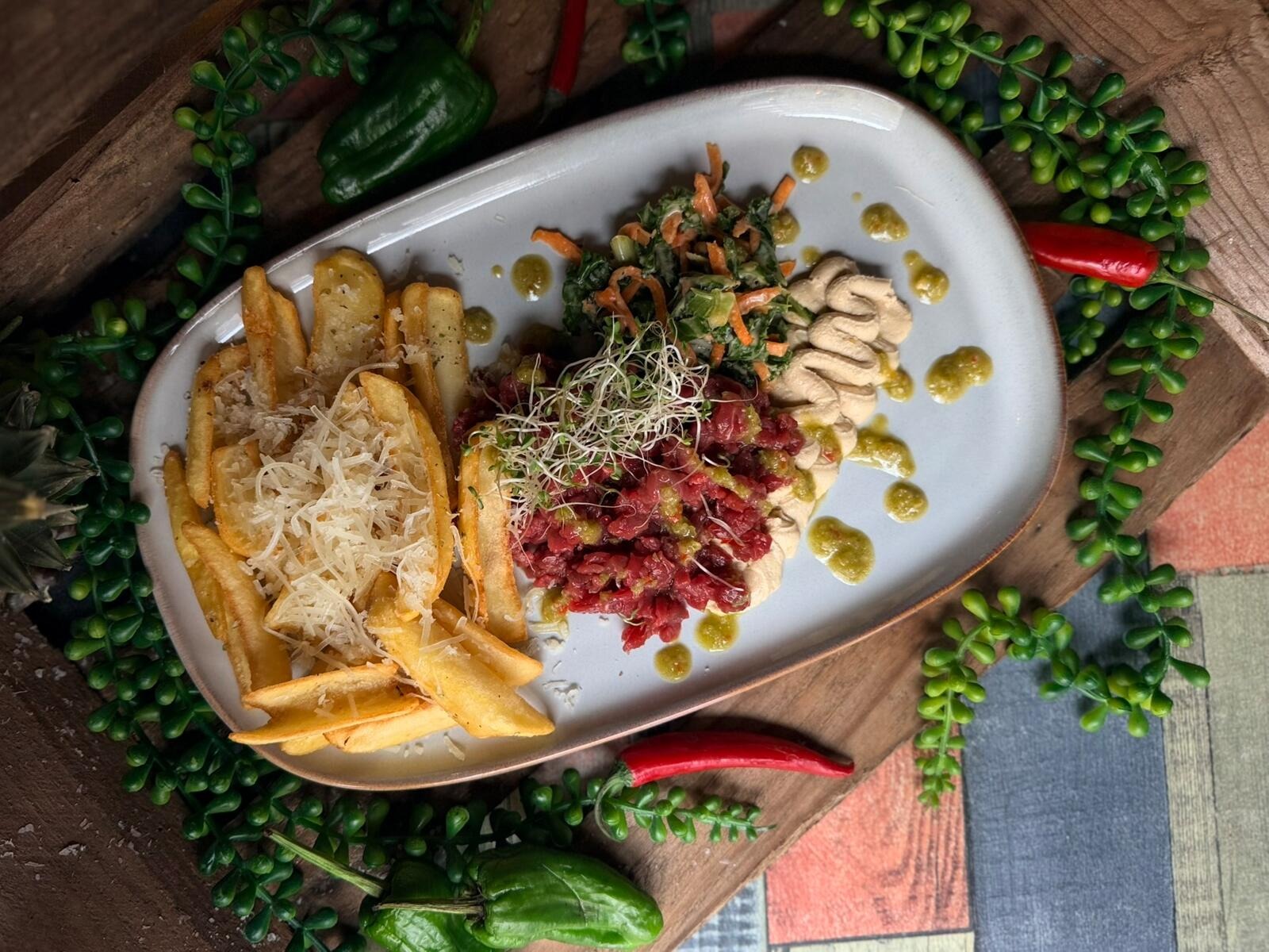 Plate with french fries, beetroot tartare, green vegetables and sliced chicken.