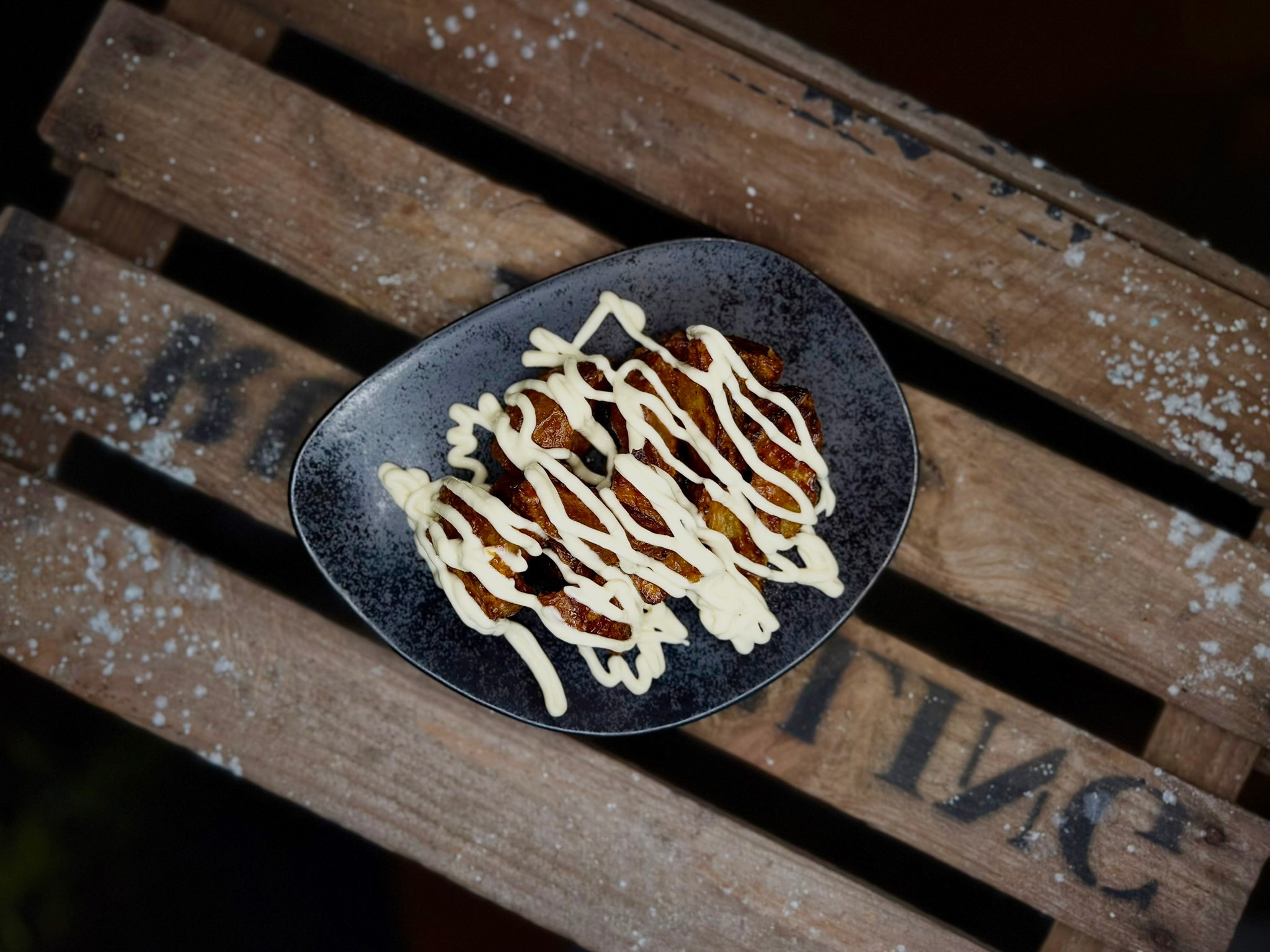 A dark blue plate holding crispy food drizzled with white sauce, placed on a wooden surface.