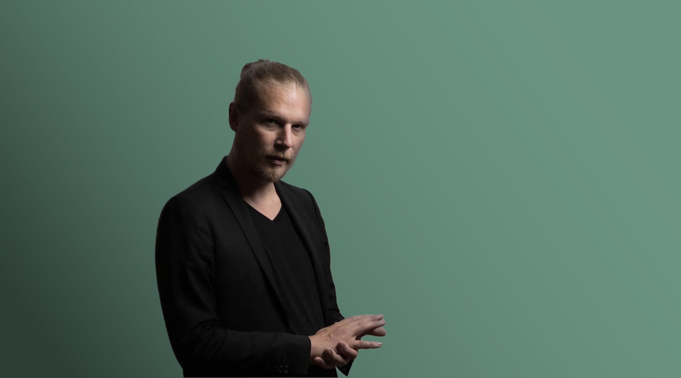 Mies seisoo vihertävän sinistä taustaa vasten.