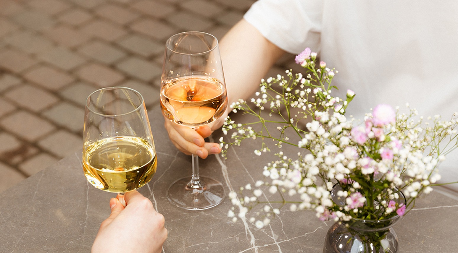 Två personer håller vinglas vid ett bord med en bukett färska blommor i en glasvas.