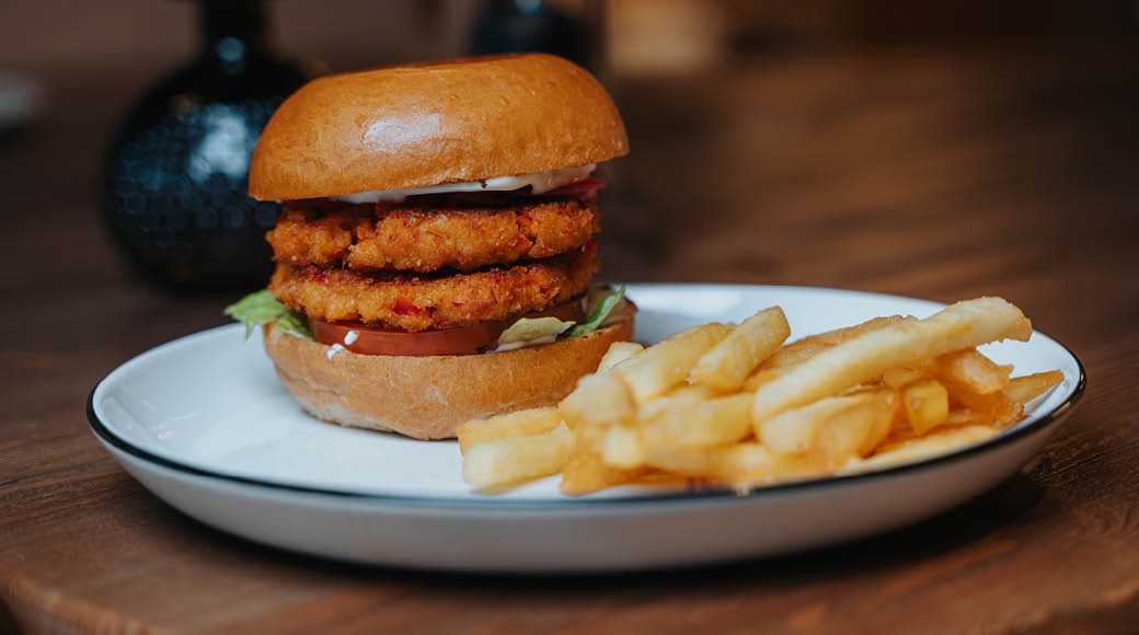 Lautasella paneroituja kasvispihvejä sisältävä hampurilainen ja ranskanperunat puisella pöydällä.