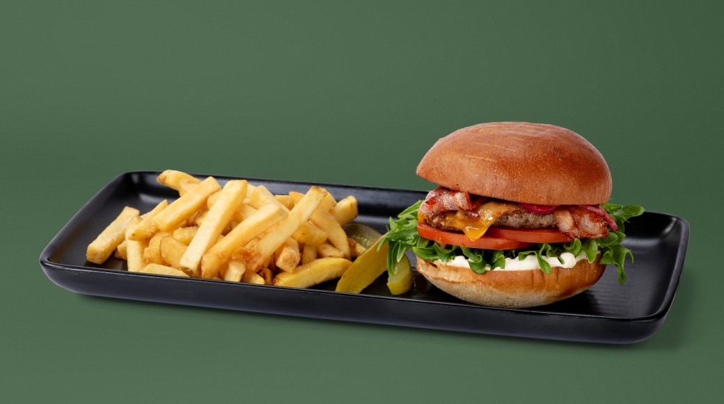 Burger and french fries on a black tray against a green background.