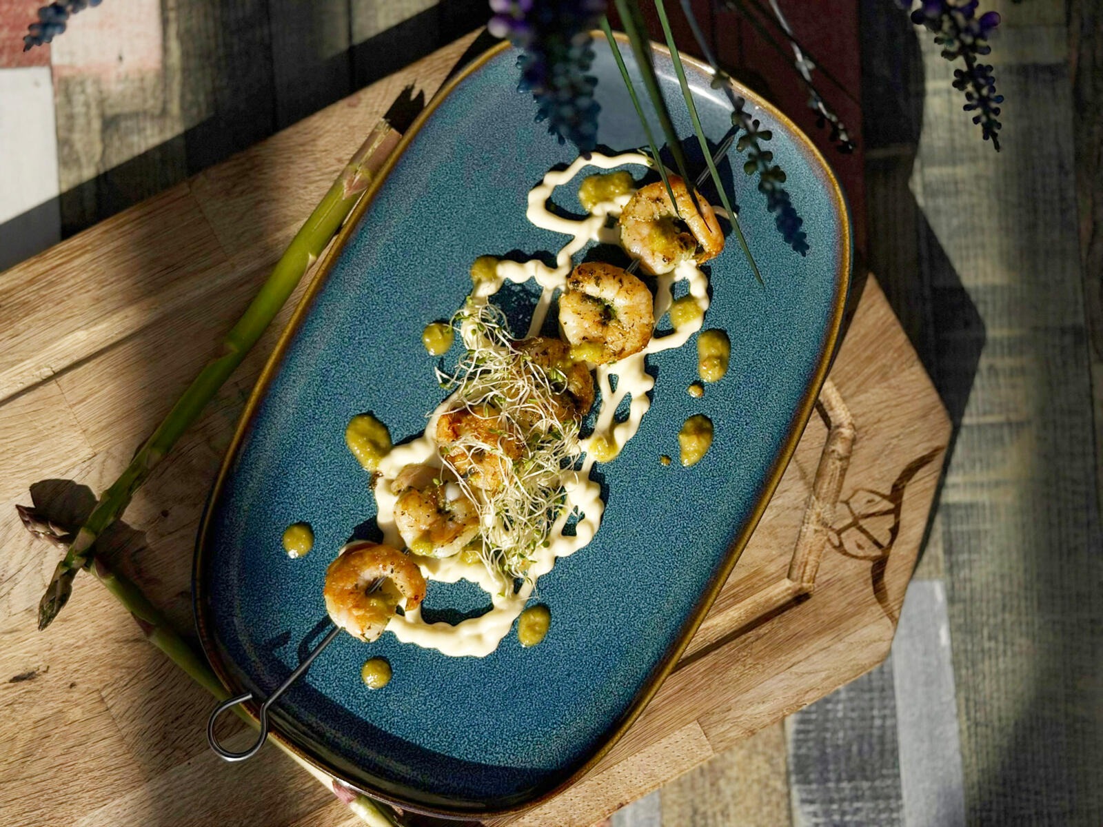 Gourmet shrimp dish on a blue oval plate, garnished with sauce and microgreens, served on wooden board.