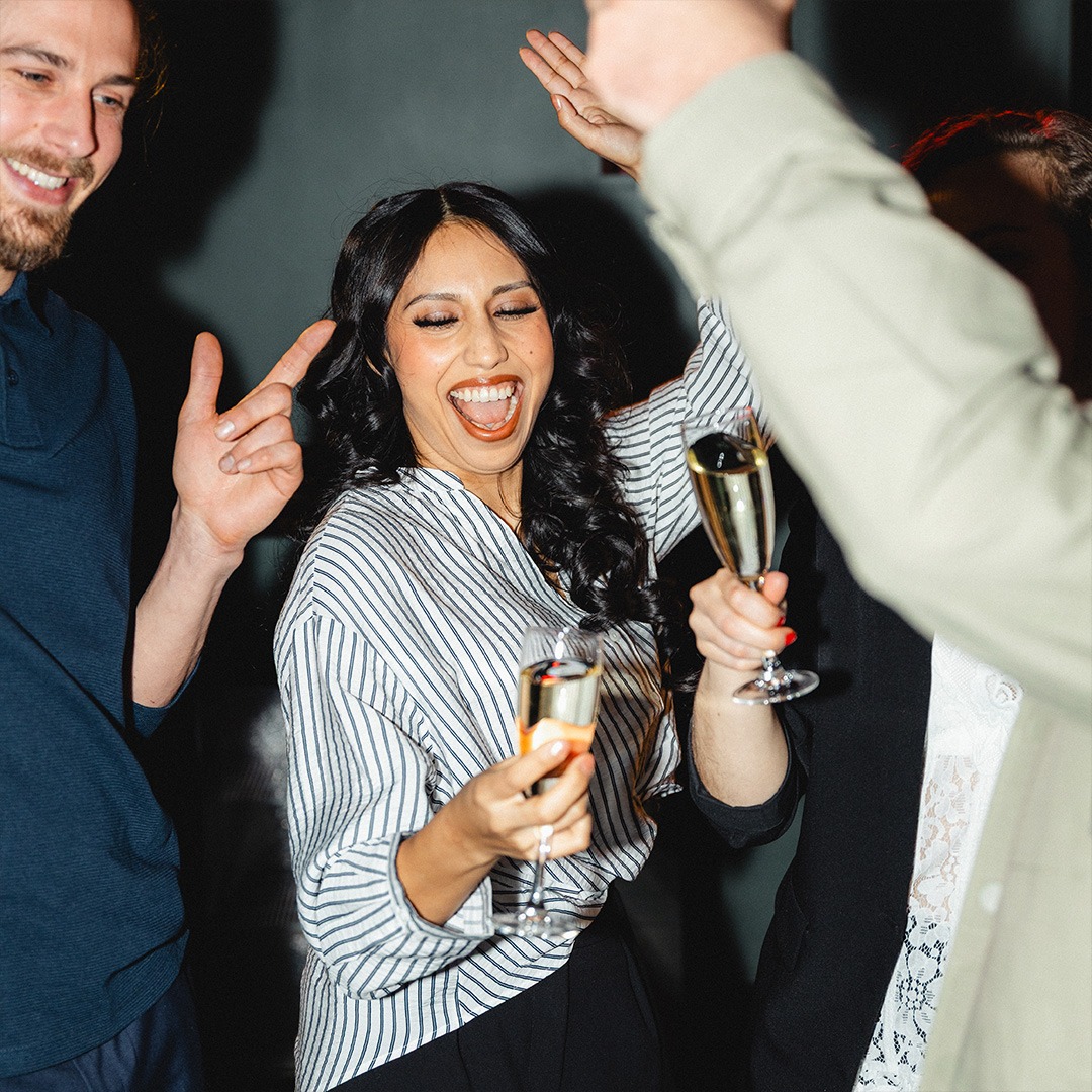 Glad kvinna firar med champagneglas i händerna omgiven av dansande personer.