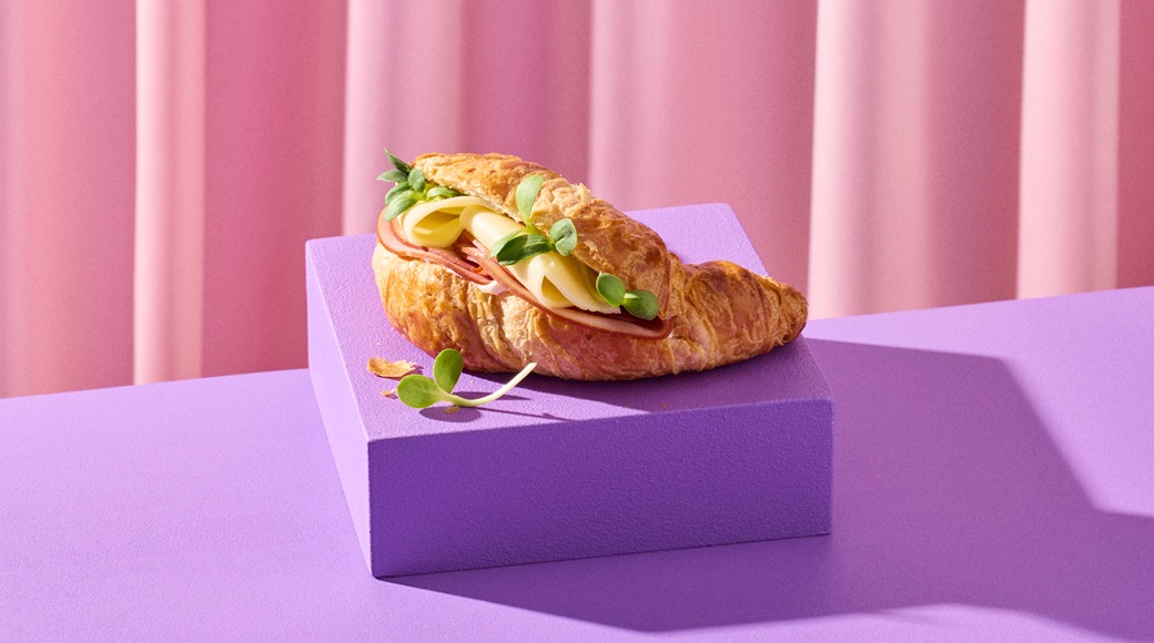 Kinkku-juustovoisarja, jonka päällä on versoja, violetilla korokkeella vaaleanpunaista verhoa vasten.
