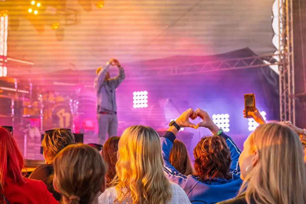 Yleisön edustaja tekee sydämen käsillään artistin tehdessä samoin. Kuvattu yleisön takaa esiintymislavalle.