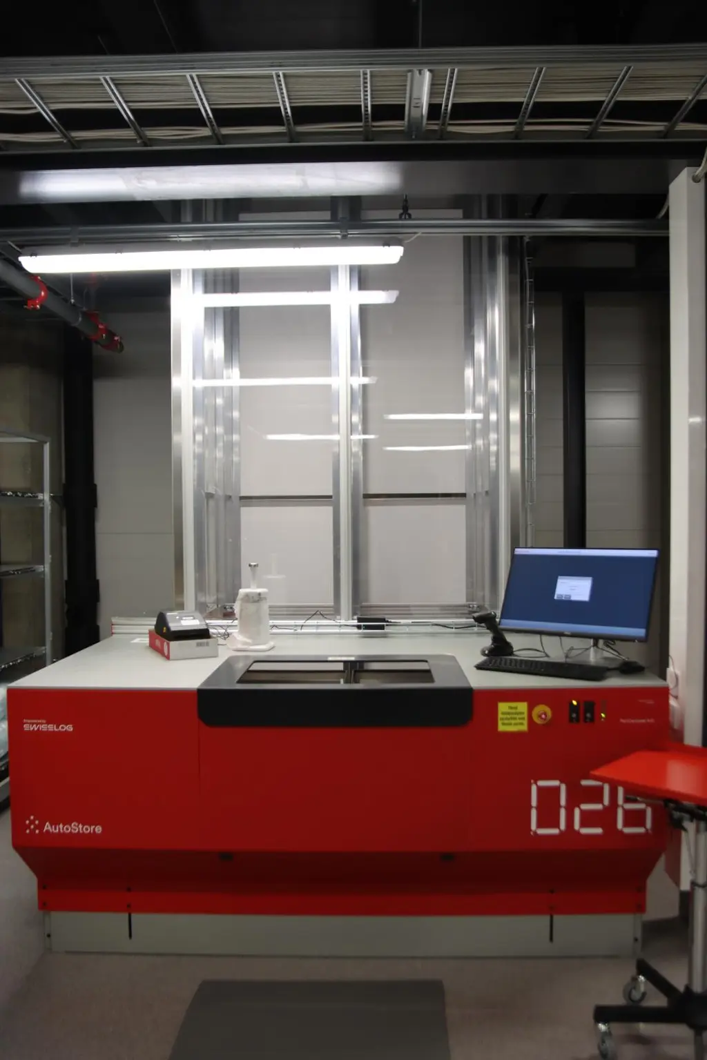 Punainen automatisoitu kone huoneessa, jossa on tietokone ja lisäpöytä.