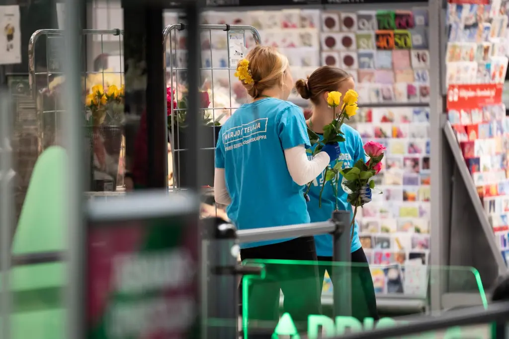 Kaksi sinipaitaista harjoittelijaa jakaa ruusuja asiakkaille.