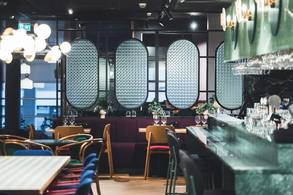 Moderni ravintola, jossa on tyylikkäitä valaistuksia, puisia tuoleja ja värikkäitä yksityiskohtia.