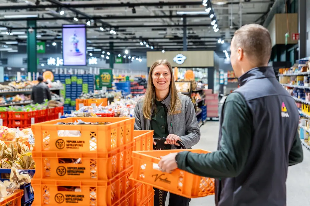 Kaksi Prisma-työntekijää leipäosastolla. Toisella on kädessään korillinen leipäpusseja.