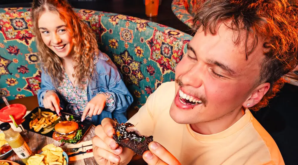 Kaksi nauravaa nuorta aikuista syömässä ravintolassa.