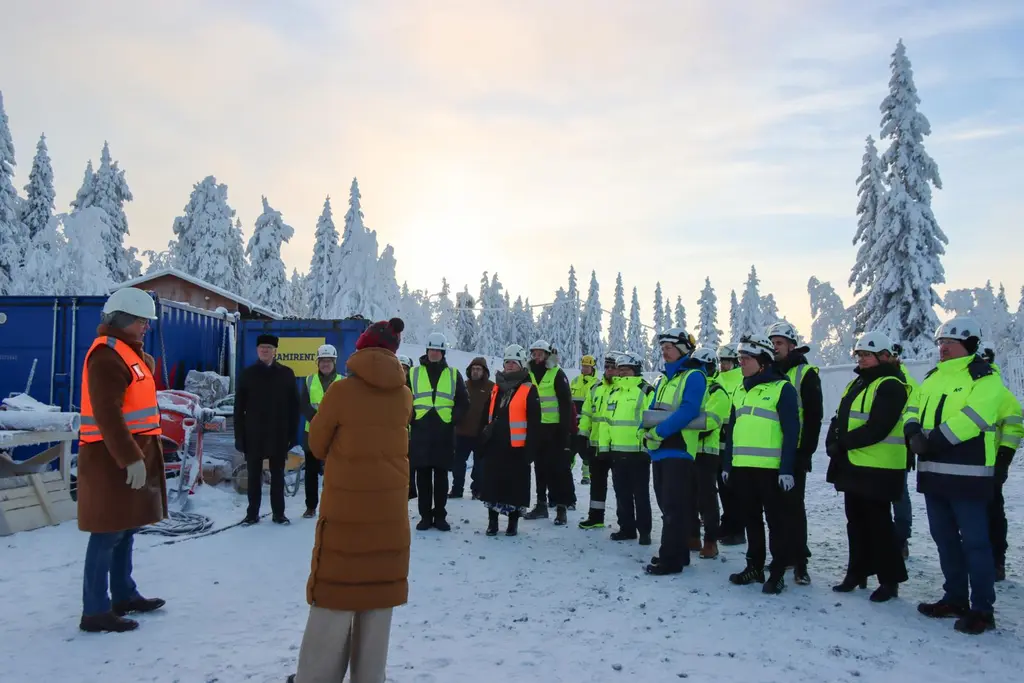 Ryhmä ihmisiä kypärissä ja huomioliiveissä seisoo lumisessa ulkotilassa.