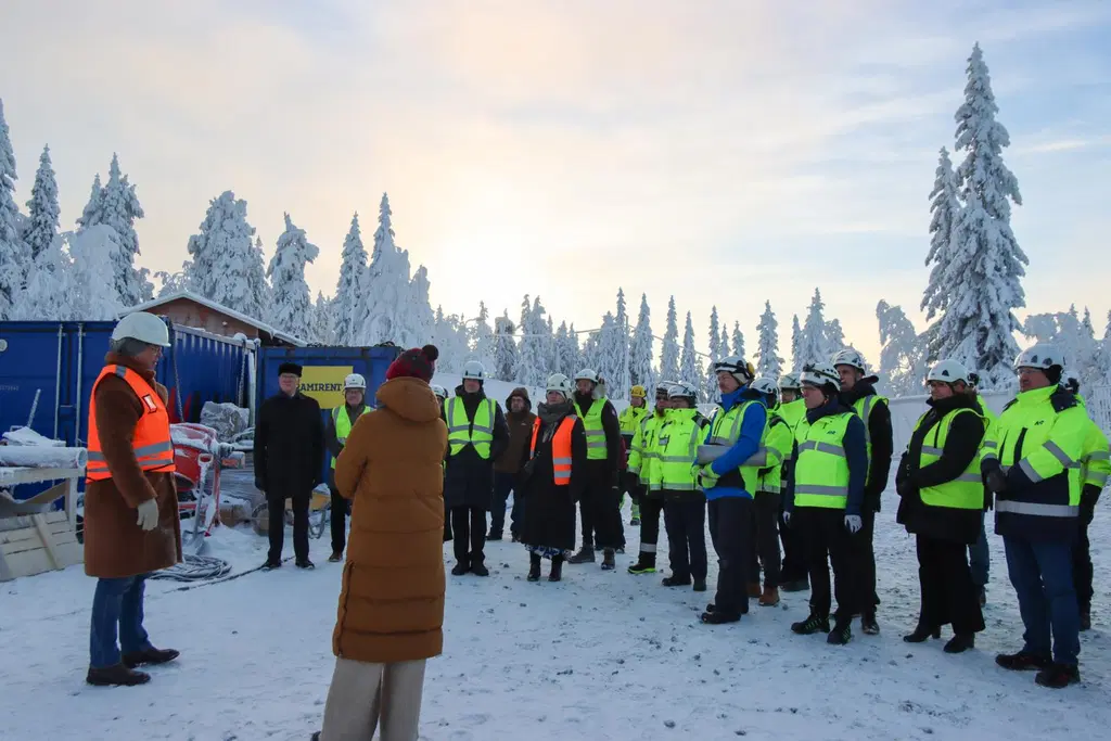 Ryhmä ihmisiä kypärissä ja huomioliiveissä seisoo lumisessa ulkotilassa.
