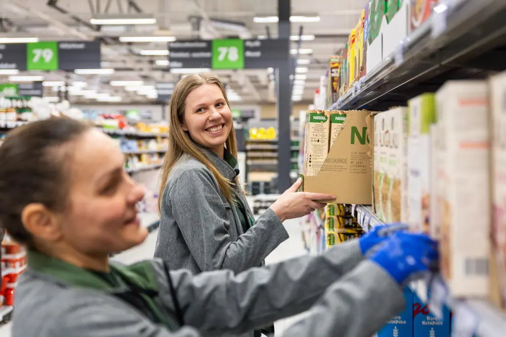 Kaksi Prisman työntekijää hyllyttää tuotteita.