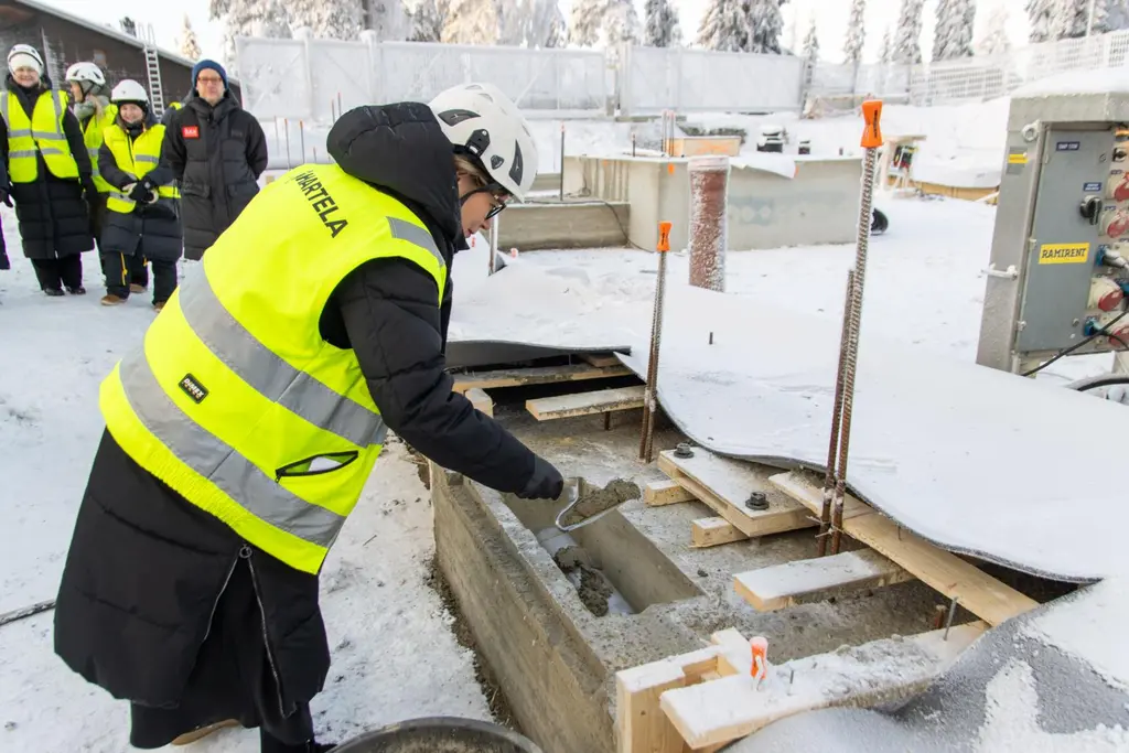 Henkilö valaa lieriön muotoista esinettä betonilaattaan talvisissa olosuhteissa.